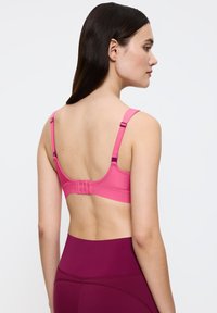 Różowy biustonosz z regulowanymi ramiączkami i solidnym zapięciem na cztery haftki z tyłu. Gładka tkanina i profilowany krój zapewniają komfort.