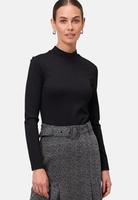 Haut noir à manches longues avec un col montant, associé à une jupe grise à motifs dotée d'une ceinture. Tissu lisse, design ajusté.