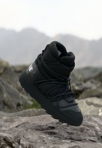 Sneaker înalt impermeabil de culoare neagră, cu țesătură texturată, guler căptușit și șireturi elastice, având un logo pe călcâi și o talpă robustă.