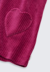 Fuchsia Kordstoff hat eine gerippte Textur mit einem herzförmigen Patch in der gleichen Farbe, der auf der linken Seite nahe dem Saum platziert ist.