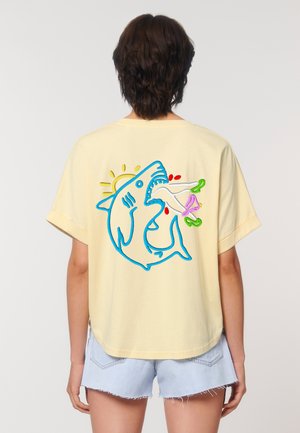 Yellow cotton t-shirt with a relaxed fit, featuring a blue embroidered shark graphic on the back, holding a stylized fish and sun.