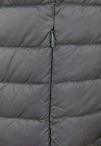 Sezione di giacca imbottita grigia con cuciture orizzontali e un piccolo dettaglio a forma di loop in tessuto sulla cucitura centrale.