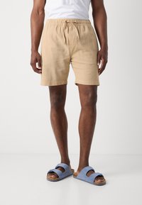 Beige bomulds shorts med elastisk talje og snøre. Sammen med blå ruskinds slip-on sandaler med dobbelt remme.