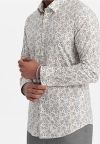 Wit longsleeve shirt met bloemenprint in oranje, grijs en groen. Heeft een kraag en knoopsluiting aan de voorkant. Gladde textuur.