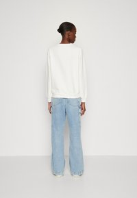 Felpa bianca con scollatura a girocollo, polsini e orlo a coste, abbinata a jeans cargo larghi di colore blu chiaro con tasche laterali e dettagli cuciti.