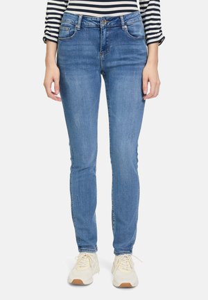 Jeans skinny blu con cinque tasche, realizzati in tessuto denim. Indossati con sneakers color avorio. Presentano una finitura leggermente sbiadita e una vita a media altezza.