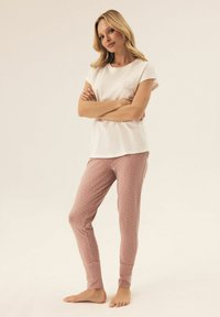 Jasnoróżowy zestaw piżamowy z bawełny, składający się z kremowej bluzki z krótkim rękawem z napisem oraz spodni w wzory z małymi ciemnymi kropkami i ściągaczami.