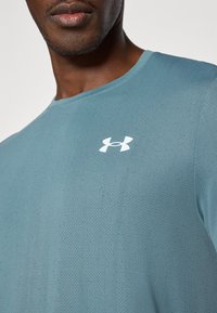 Hele sinine sportlik särk, mis on valmistatud tekstuuriga kangast, millel on ümmargune kaelus ja väike valge logo rinnal.