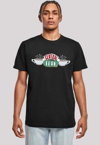 Melns kokvilnas T-krekls ar "Central Perk" logo, kurā ir divas baltas kafijas krūzes un tvaiks virs tām, parādīts uz viendabīga fona.