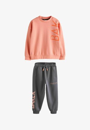 Hele roosa pusa, millel on "BAK" graafika, kombineeritud tumehallide dressipükstega, millel on "BAKER" trükk. Valmistatud pehmest ja mugavast kangast.