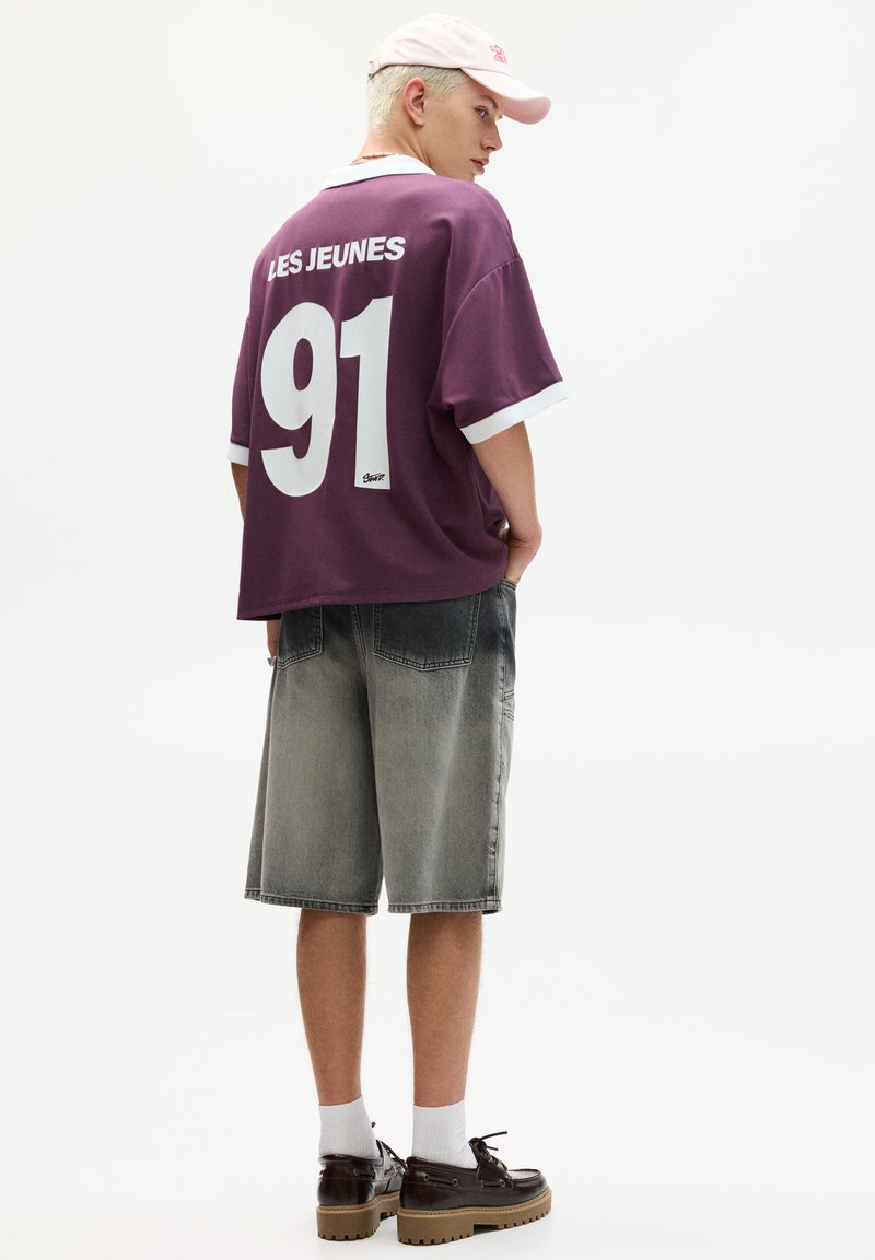 Oversized purple jersey with white accents, "LES JEUNES" and "91" on the back. Paired with gray denim shorts and brown shoes.