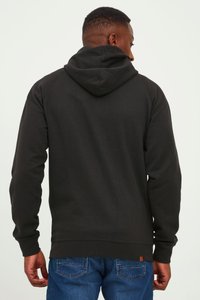 Black hoodie with a drawstring hood and ribbed cuffs. Worn with blue denim jeans featuring a stitched mountain pattern on the pockets.