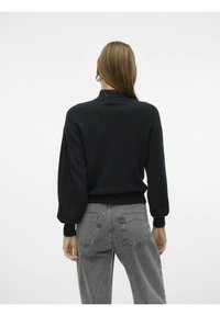 Svart stickad tröja med hög krage, ribbade ärmslut och en avslappnad passform, kombinerad med grå jeans med hög midja och bakfickor.