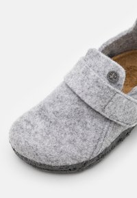 Szare buty wsuwane z filcu, z rzepem, teksturowanym wierzchem i czarną gumową podeszwą. Zauważalny okrągły detal logo na rzędzie.