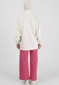 Maglietta bianca a maniche lunghe con colletto alto, abbinata a pantaloni rosa larghi e fin sopra il ginocchio. Tessuto morbido con una silhouette rilassata.