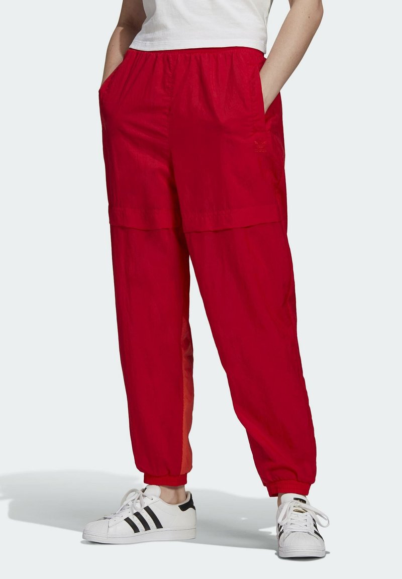 Röda lätta byxor med elastisk midja, sidofickor och mudd kring bensluten. Bärs med vita sneakers med svarta ränder.