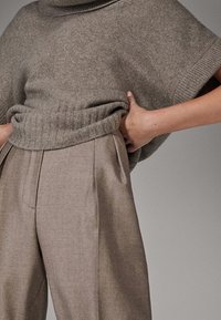 Harmaa neulottu villapaita leveällä kaula-aukolla, yhdistetty beigeihin korkeavyötäröisiin housuihin, joissa on terävät laskokset ja sivutaskut.