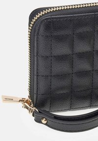 Cartera de piel texturizada negra con cremallera dorada y tira de agarre con la marca GUESS, que incluye una pequeña correa de muñeca con botón dorado.