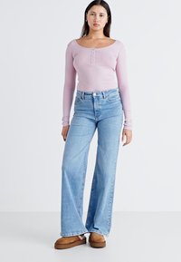 Lyserosa ribbestrikket langermet topp med knappefront, parret med lyseblå vide jeans og brune slip-on sko.