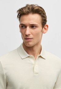 Polo shirt beige chiaro realizzato in tessuto testurizzato. Caratterizzato da un colletto classico e un logo ricamato discreto sul petto.