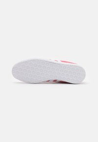 Shoe with a red upper featuring three white stripes, rubber sole with a textured pattern, and a rounded toe design.