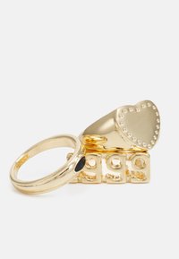 Anéis em tom dourado com um topo em forma de coração com contas elevadas, uma faixa adicional com um detalhe preto e uma base decorada.