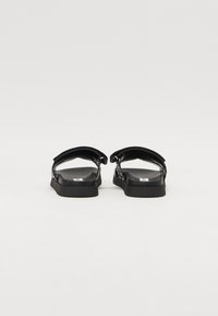 Schwarze Sandalen mit flacher Sohle und dicken Riemen. Das Design umfasst Kettenakzente, hat eine glatte Oberfläche und eine offene Ferse.