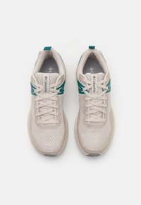 Beige athletic shoes with mesh upper, teal accents, round toe, and rubber sole. Features laces and logo on tongue.