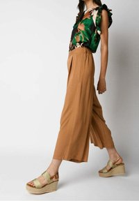 Blouse à motifs floraux avec des manches volantées, associée à un pantalon beige à jambes larges et des sandales à talons compensés vert clair avec des accents de lanières.