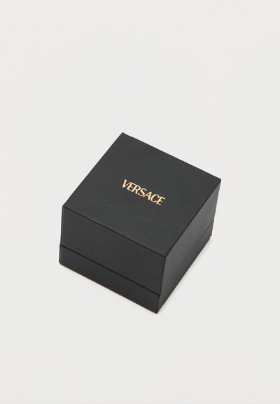 Μαύρο τετράγωνο κουτί με υφή και χρυσό λογότυπο "VERSACE" στο κέντρο στην κορυφή, σε λευκό φόντο.