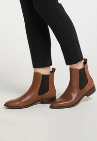 Ruskeat nahkaiset Chelsea-saappaat, joissa on joustavat sivupaneelit, teräväkärkiset kärjet ja teksturoitu yksityiskohta kantapäässä. Yhdistetty mustiin slim fit -housuihin.