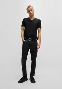 Sort v-hals t-shirt parret med sorte slim-fit bukser og sorte sneakers. Har et glat, let stof og en struktureret design.