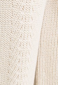 Tissu tricoté couleur crème présentant deux motifs texturés distincts avec des mailles côtes verticales et diagonales finement détaillées.