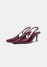 Décolleté in vernice bordeaux con punta affusolata, tacco basso e lati ritagliati per una silhouette elegante. Cinturino regolabile con fibbia.