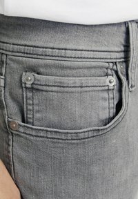 Jean en denim gris avec une petite poche avant, des boutons en métal argenté et une surface en tissu texturé. Design ajusté sans embellissements.