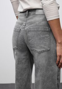 Jeans in denim grigio con vita alta, dotati di due tasche posteriori e una leggera sfumatura. Il tessuto ha una consistenza morbida e dettagli di cucitura minimi.
