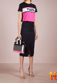 Black and pink t-shirt with "KARL" logo, paired with a black pencil skirt featuring a slit and side stripes. Holding a black and pink handbag.