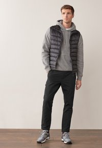 Veste noire matelassée portée sur un sweat à capuche gris, associée à un pantalon noir et des baskets grises. Textures lisses et coupe décontractée. Détails subtils tels que des fermetures éclair.