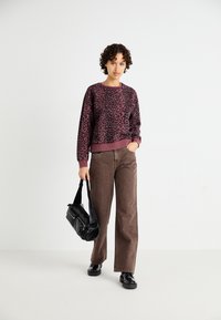 Bordó leopárd mintás pulóver bordás mandzsettával, barna bővülő nadrággal és fekete platform cipővel párosítva. Fekete kézitáska is tartozik hozzá.