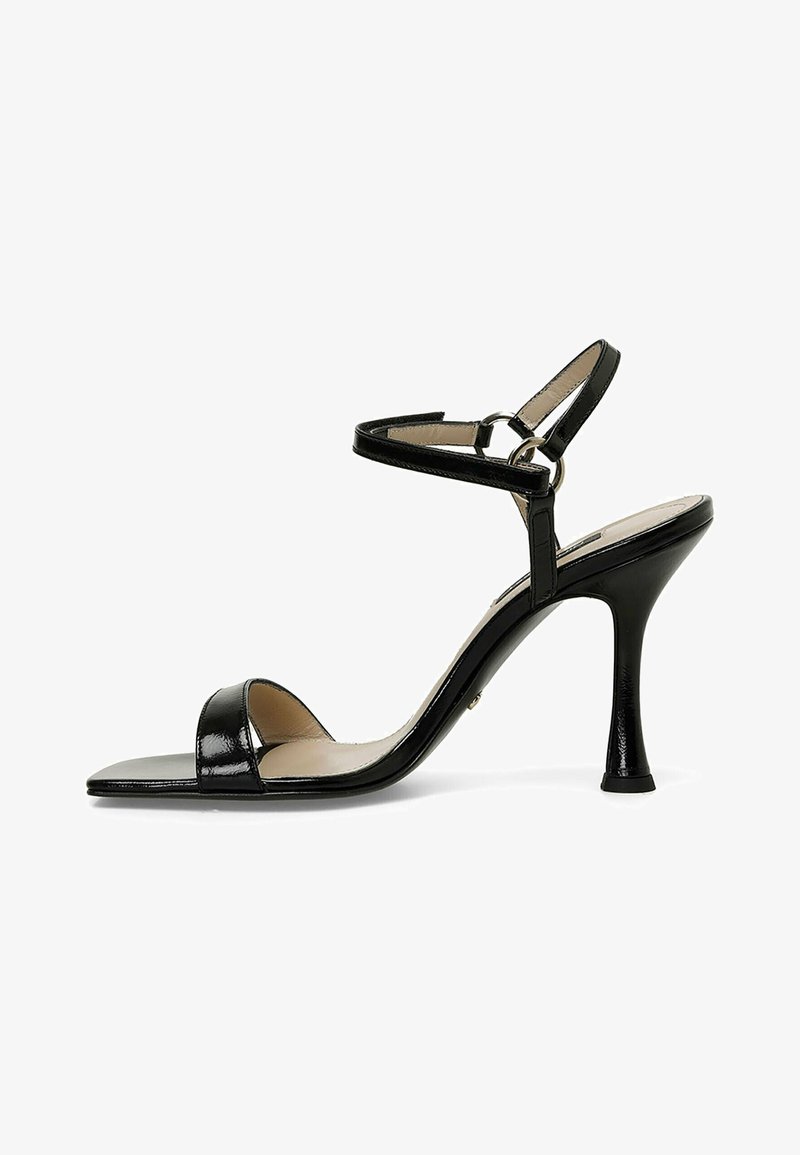 Sandalias de tacón alto de charol negro con puntera cerrada, tira en el tobillo y un acento metálico en el tacón, que presentan un diseño elegante y minimalista.