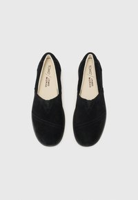Scarpe slip-on nere in suede con punta rotonda, caratterizzate da cuciture discrete e inserti elastici laterali per una facile calzata. Il marchio interno è visibile.