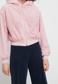 Rosa fodrad zip-up hoodie med en åtsittande midja och ärmslut, med huva och sidofickor för ökad detalj och komfort.