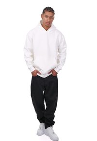 Hvid hættebluse med frontlomme, parret med sorte løstsiddende bukser og hvide sneakers. Glat stof med en afslappet pasform.
