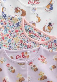 Trois vêtements pour enfants ornés de motifs ludiques de cobayes. Les tissus sont en coton blanc, rose et lavande avec des accents floraux.