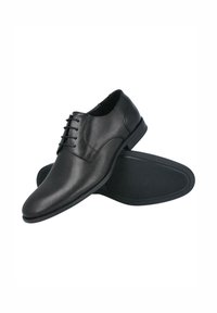 Zapatos de vestir de cuero negro con superficie lisa y detalles perforados. Presentan un diseño con cordones y una suela de goma con perfil plano.