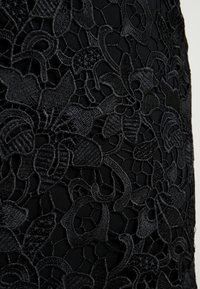 Tissu en dentelle noire avec une broderie florale complexe. La texture présente un motif en mesh avec des formes et motifs floraux variés.