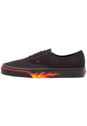 Zapatilla Vans negra con diseño de llamas rojas y amarillas en la suela y cordones negros, mostrada de perfil sobre fondo blanco.