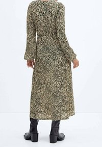 Robe midi à manches longues avec un motif à pois vert et crème, présentant une silhouette fluide et associée à des bottes noires jusqu'aux genoux.