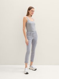 Débardeur gris clair, pantalon gris clair taille mi-haute avec cordon de serrage, coupe ajustée, longueur cropped, associé à des baskets blanches avec accents noirs.
