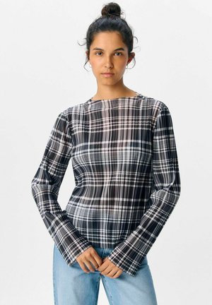 Langmouw zwart-wit geblokt top met een ronde halslijn, licht doorzichtige stof en uitlopende mouwen. Draagt het bij lichte blauwe jeans.